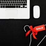 Stylish flat lay of a laptop, mouse, and sale tag on a hanger for online shopping concept.