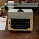 A classic workspace featuring a 70s typewriter, rotary phone, and documents on a wooden desk.