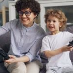 A mother and son smiling and playing video games on a sofa indoors.